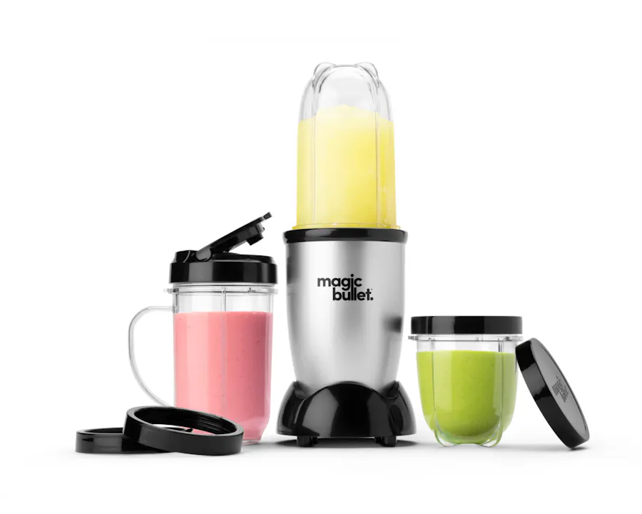 Silver magic bullet blender with yellow smoothie cup alongside pink and green smoothie containers and accessories.