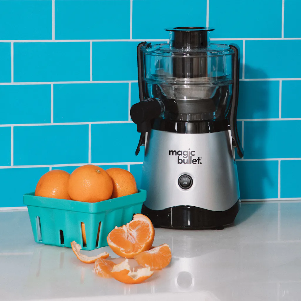magic bullet Mini Juicer magic bullet Mini Juicer on kitchen countertop with turquoise background alongside fresh oranges