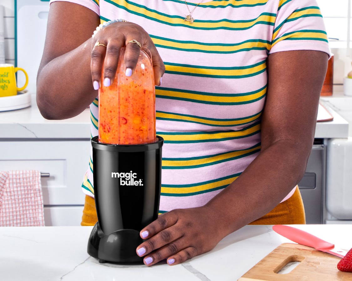 magic bullet black blending a orange smoothie in the kitchen
