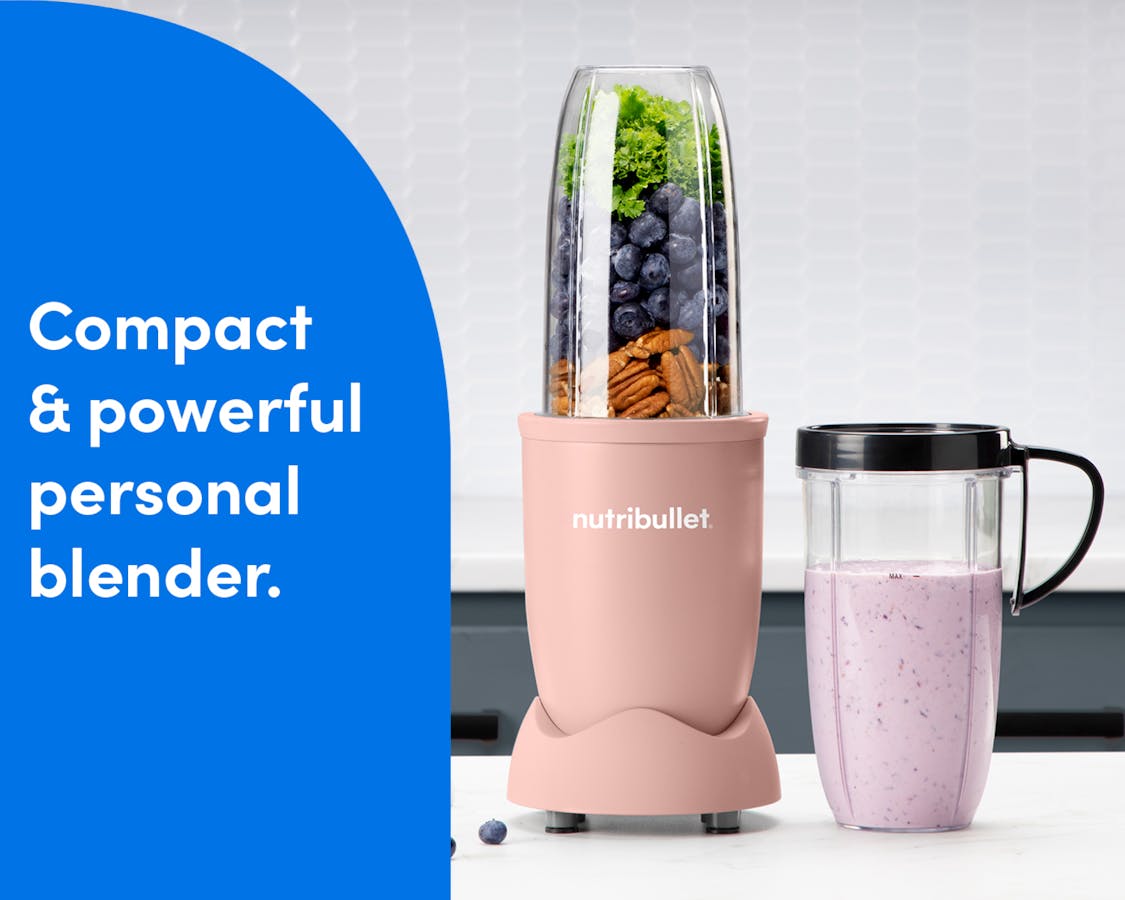 The nutribullet Pro rests on a white countertop. The Tall Cup is attached to the Power Base and filled with a variety of unblended fruits and vegetables. A Tall Cup with the Handled Lip Ring attached rests to the right of the blender, filled with a light pink smoothie.