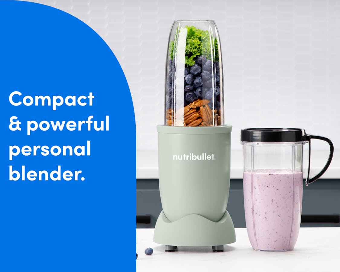 The nutribullet Pro rests on a white countertop. The Tall Cup is attached to the Power Base and filled with a variety of unblended fruits and vegetables. A Tall Cup with the Handled Lip Ring attached rests to the right of the blender, filled with a light pink smoothie.