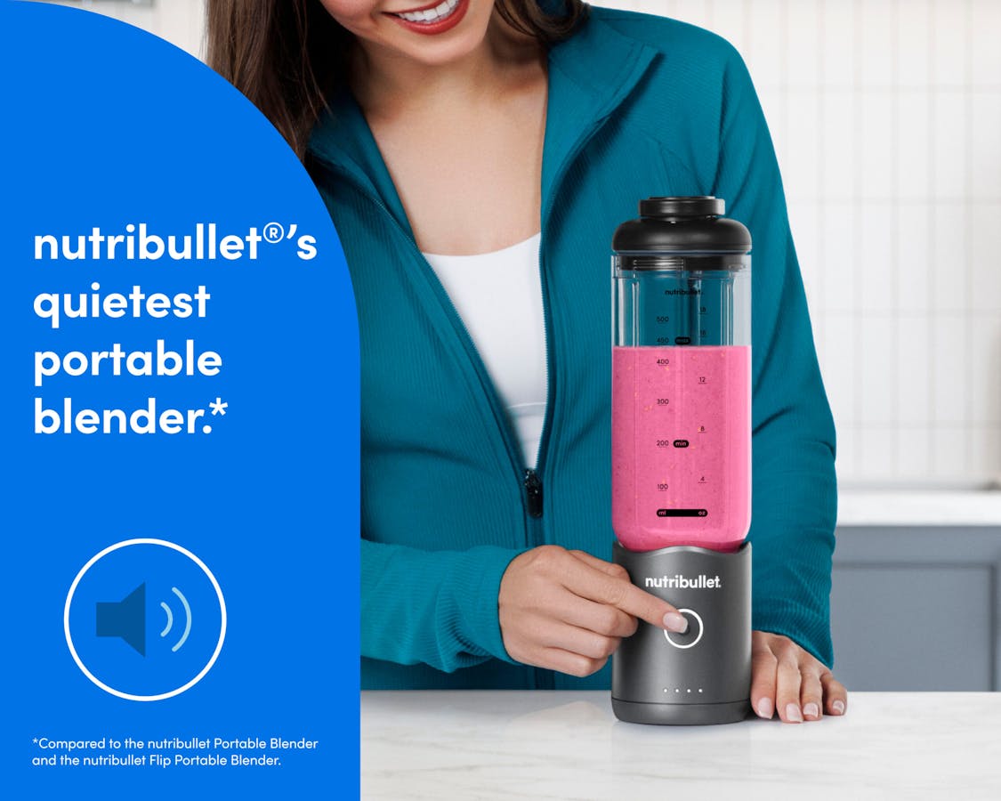 nutribuleet Flex - quieter portable blending A woman in a teal zip-up athletic jacket presses the blend button on the bottom of the motor base to blend a bright pink smoothie.