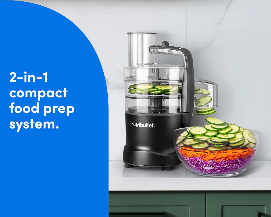 The Black nutribullet Limitless Food Processor on a kitchen counter slicing cucumbers beside a colorful salad bowl.