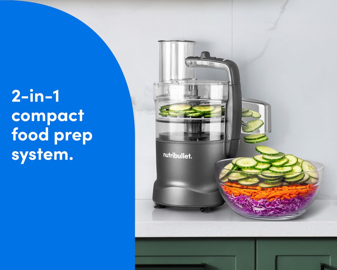 The Gunmetal nutribullet Limitless Food Processor on a kitchen counter slicing cucumbers beside a colorful salad bowl.