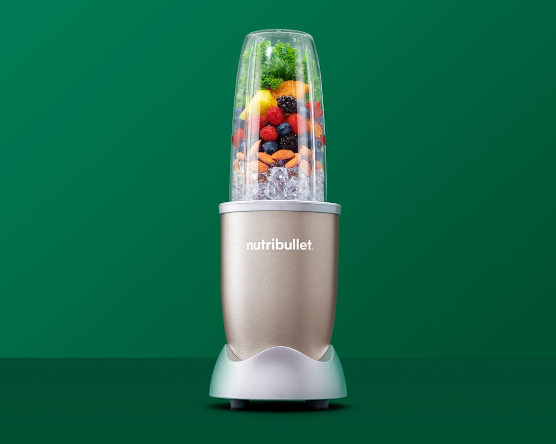 nutribullet Pro Champagne with fruits, vegetables, and nuts on green background.