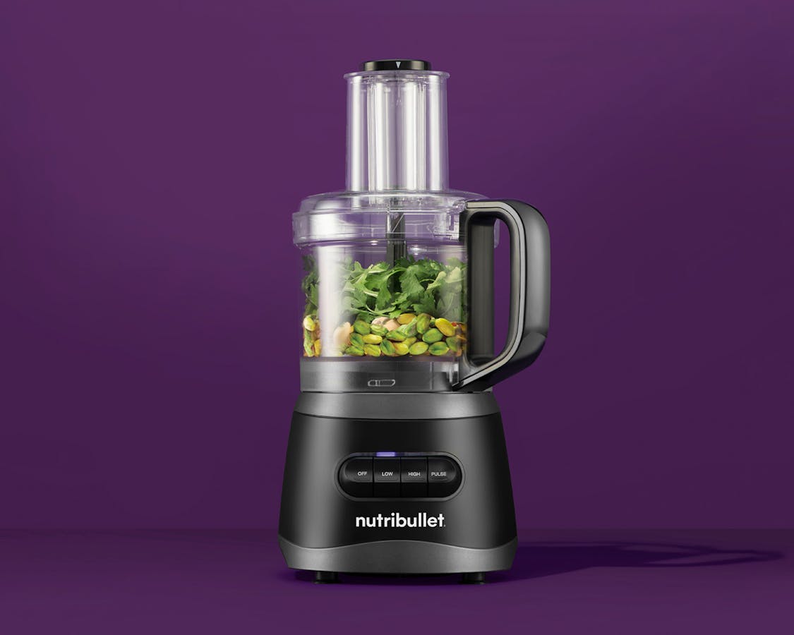 nutribullet® 7-Cup Food Processor with black motor base and black handle filled with green vegetables and nuts against a purple background
