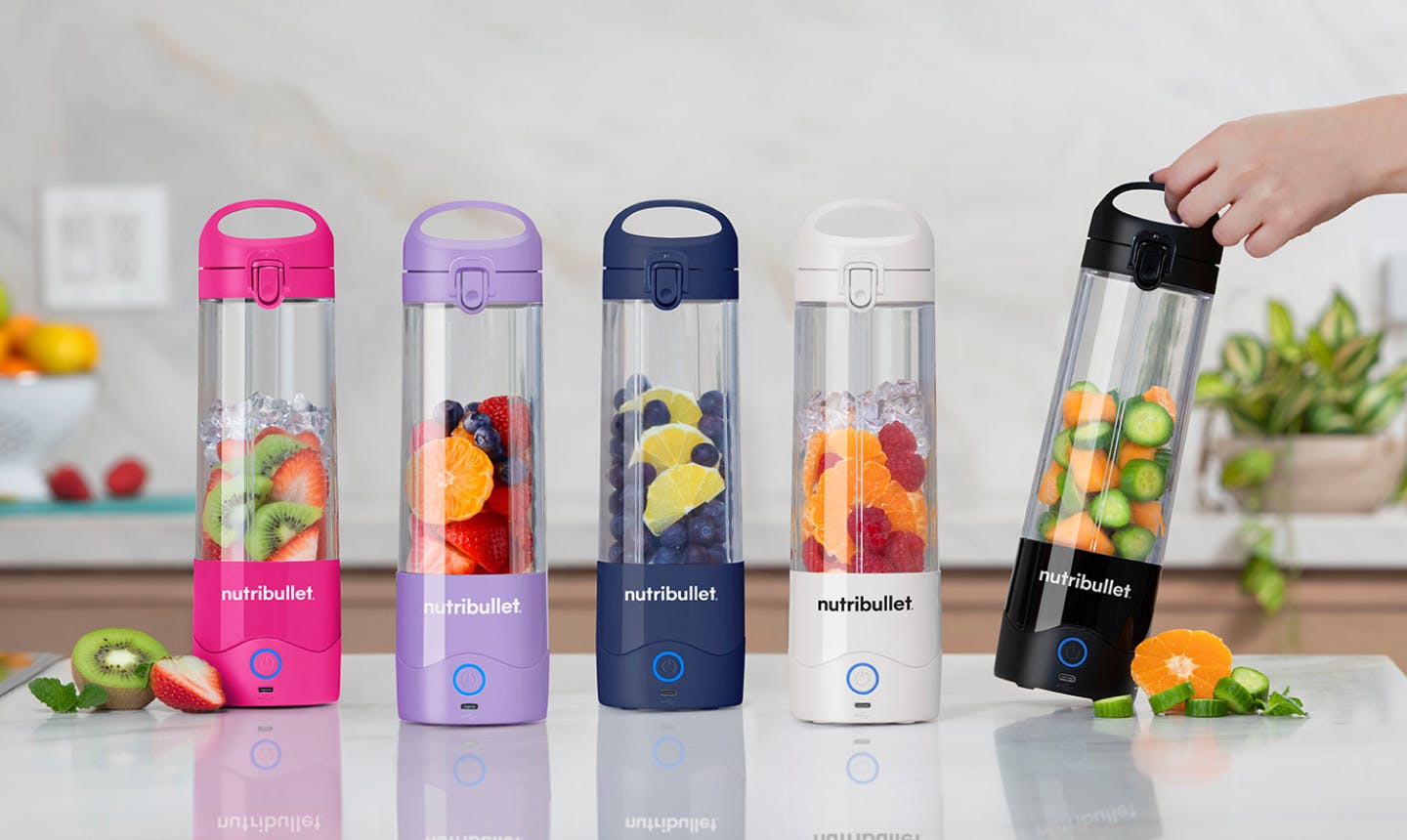 NutriBullet portable bottles in various colors (pink, purple, blue, white, and black) filled with fresh fruits and vegetables, placed on a kitchen countertop