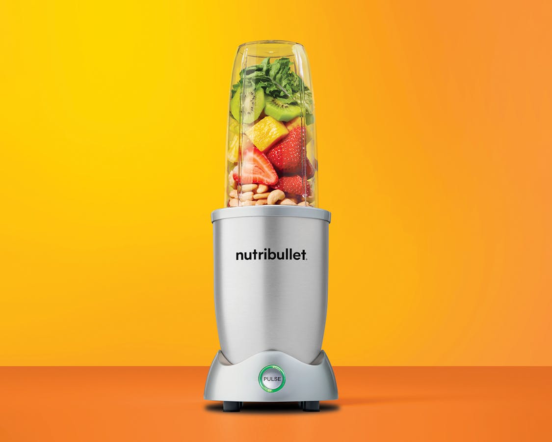 Silver nutribullet Pro+ blender filled with berries, pineapple and banana on white countertop.