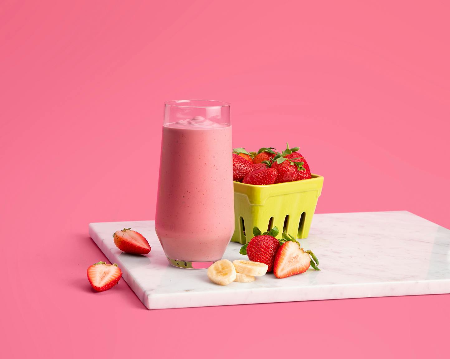 Pink strawberry smoothie on marble cutting board with pink background