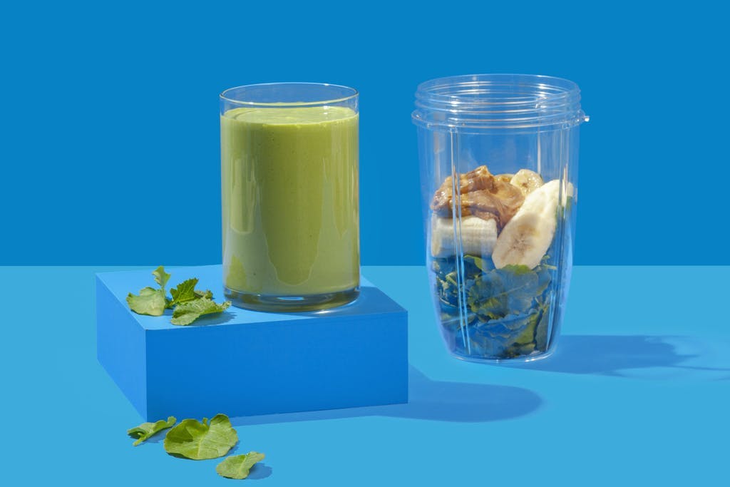 green smoothie in a glass with spinach, banana, and nut butter in NutriBullet cup