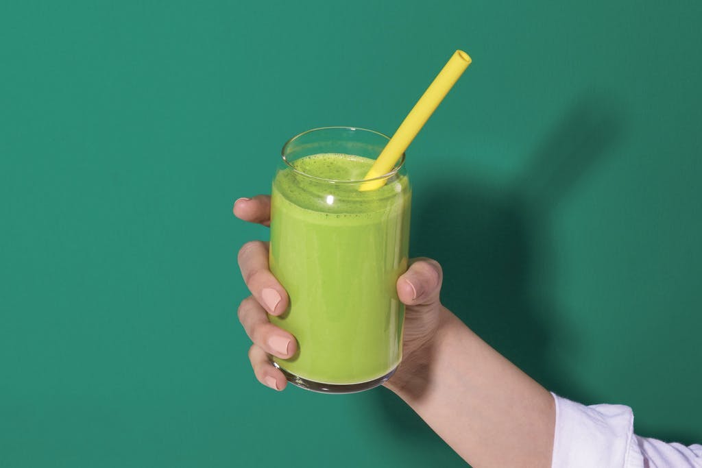 handing holding up green smoothie again green background