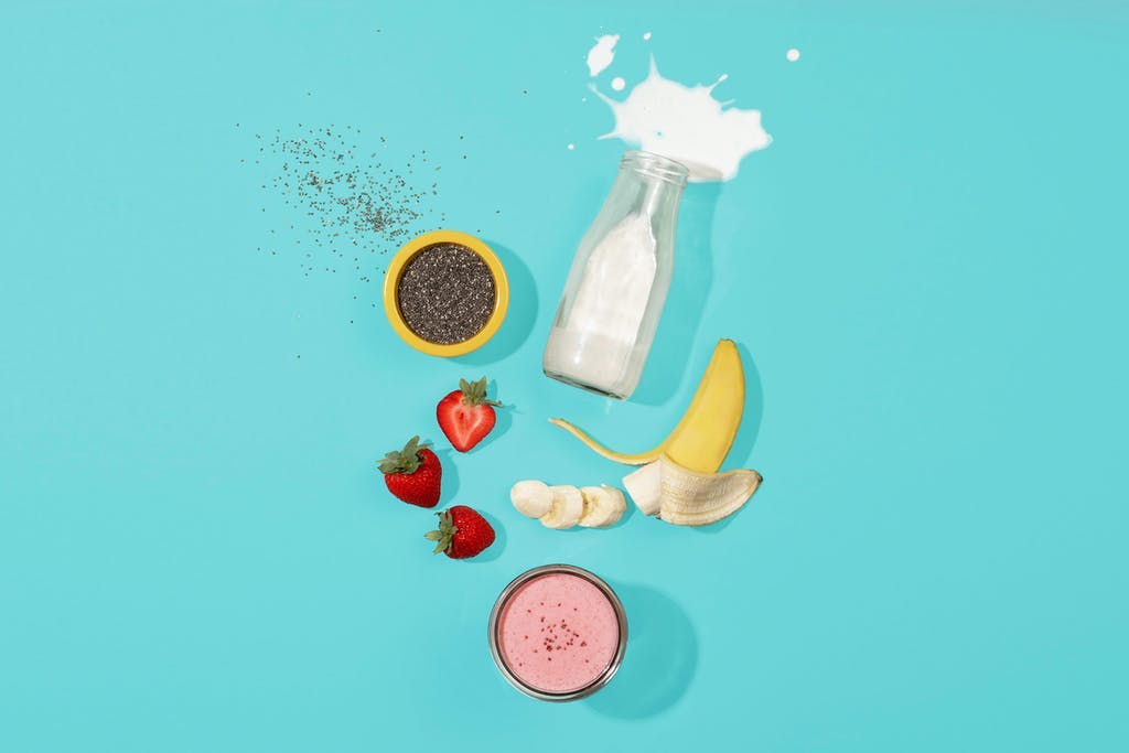 pink smoothie flatlay with strawberries, banana, chia seeds, and almond milk