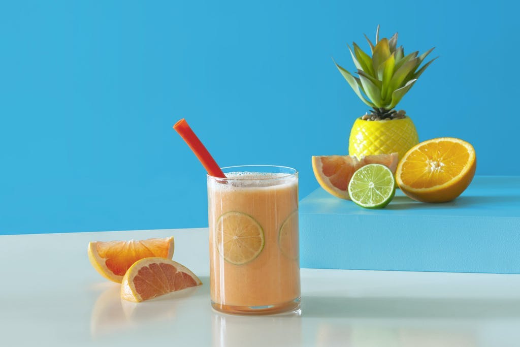 orange smoothie with lime slices in a glass surrounded by cut grapefruit, orange, and lime