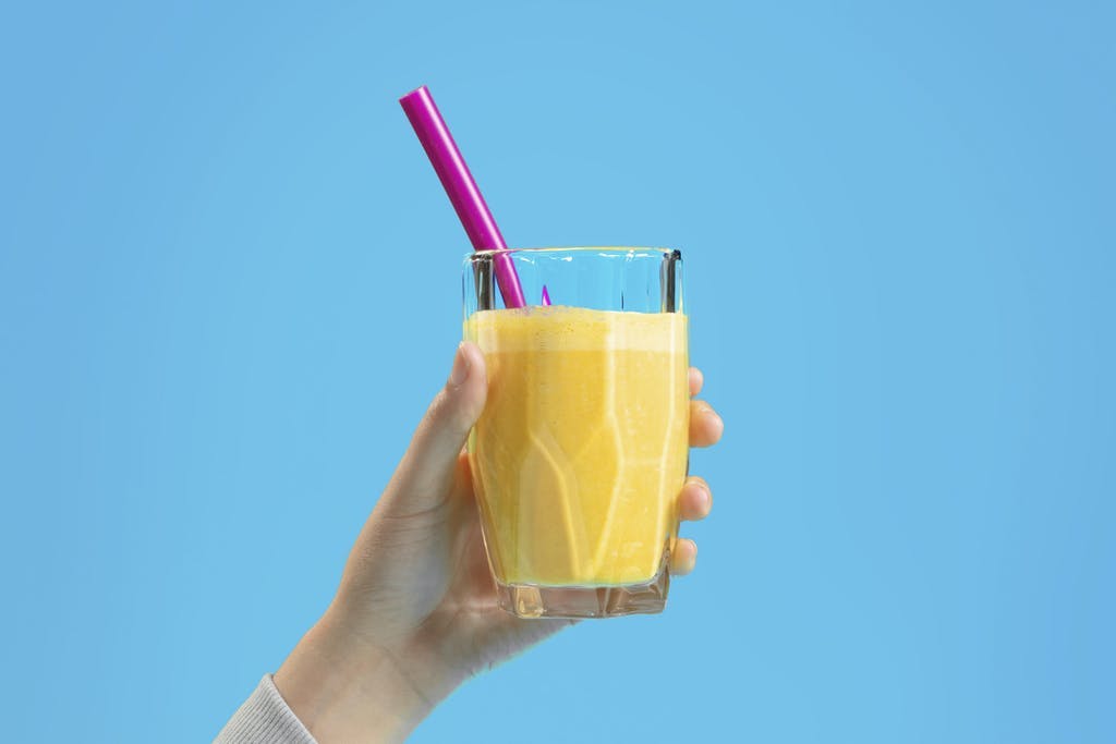 hand holding up a glass of vibrant yellow tropical smoothie