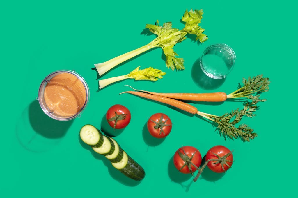 orange vegetable smoothie flatlay with celery, tomatoes, carrots, and cucumber