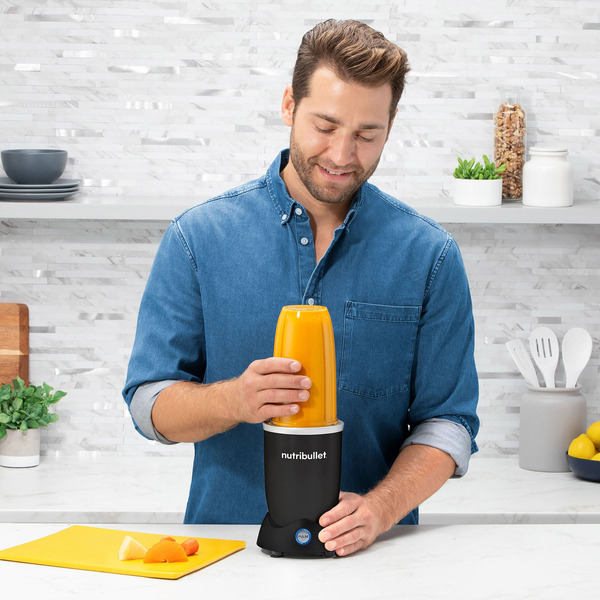 man blending orange smoothie in a black nutribullet Pro+ in a kitchen