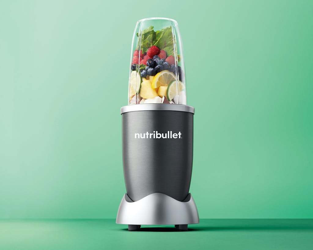 nutribullet original with fruit and vegetables on green background.
