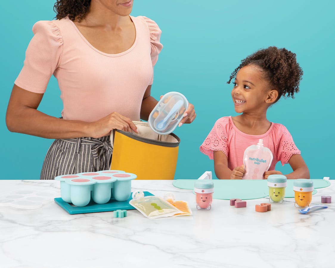 Woman with young girl with assorted nutribullet Baby products with a blue background.