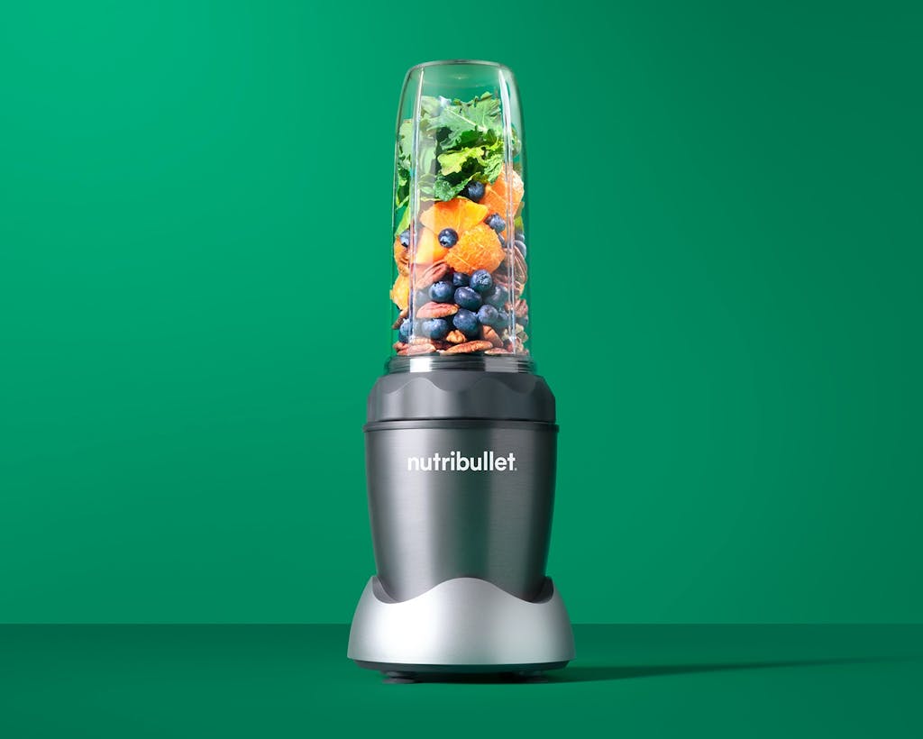 nutribullet PRO 1000 with fruits, vegetables, and nuts on green background.