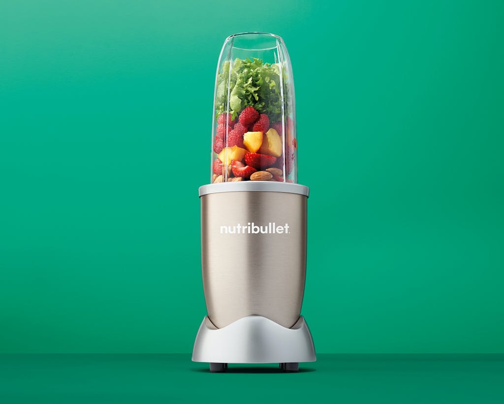 NutriBullet Pro Champagne with fruits, vegetables, and nuts on green background.