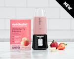 Product preview 1 of 3. Thumbnail of black nutribullet Go filled with pink smoothie next to pink strawberry banana smoothie package on counter.
