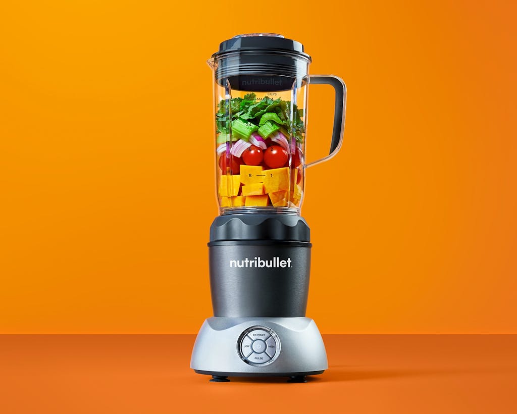 nutribullet Select with fruits and vegetables on orange background.