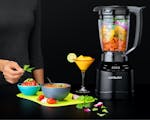 Product preview 3 of 8. Thumbnail of black nutribullet Smart Touch blender filled with fruit next to a spread of food and drink on black background.