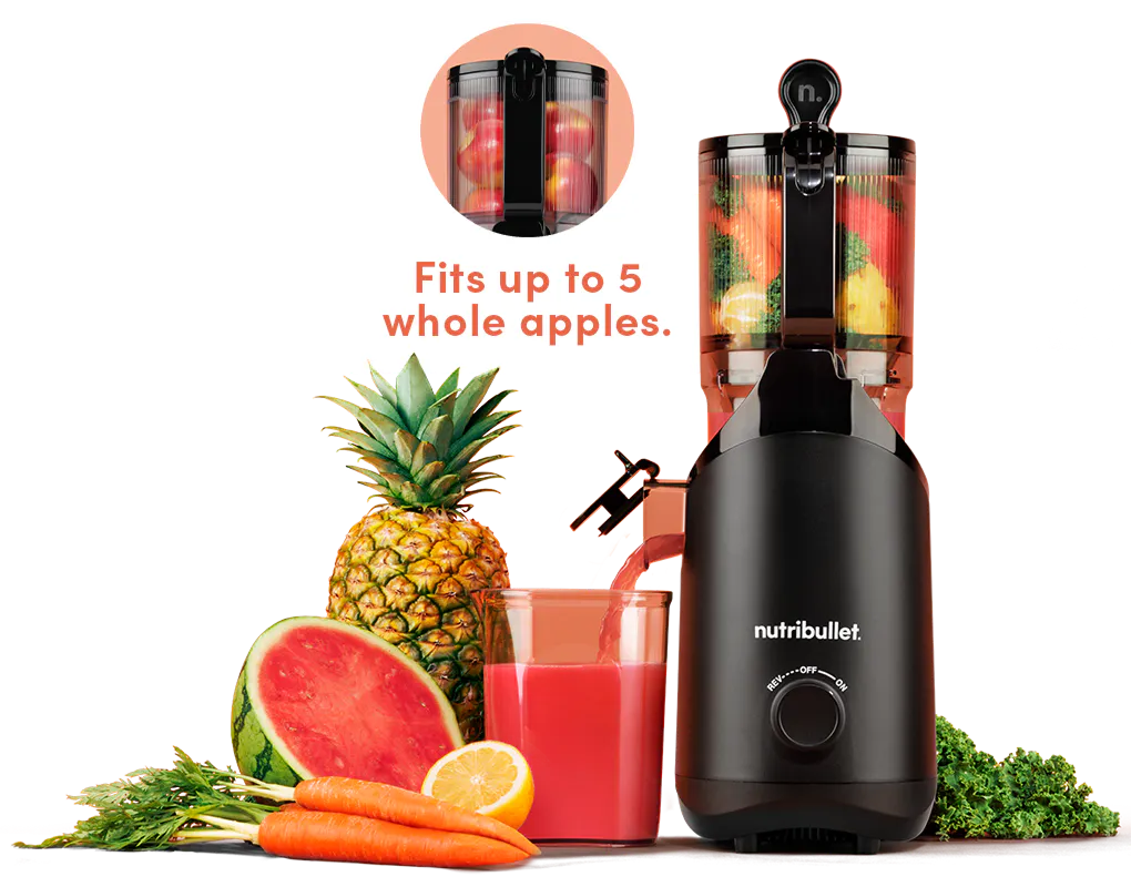 Black nutribullet Cold Press Juicer filled with carrots, kale, and lemon, pouring red juice into a glass next to watermelon, pineapple, and carrots on a marble counter.