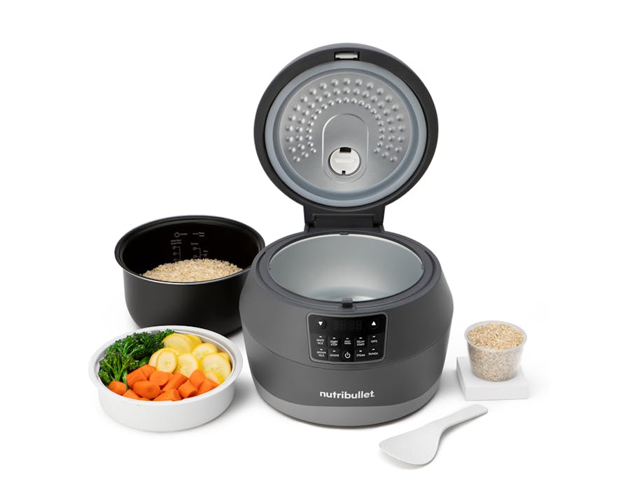 The nutribullet EveryGrain Cooker with an open lid, displayed alongside a bowl of vegetables, a cup of rice, and a serving spoon, designed for cooking various types of grains.