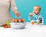 Product preview 1 of 8. Thumbnail nutribullet Baby Steamer with eggs next to fruits and veggies with mother's hand and baby.