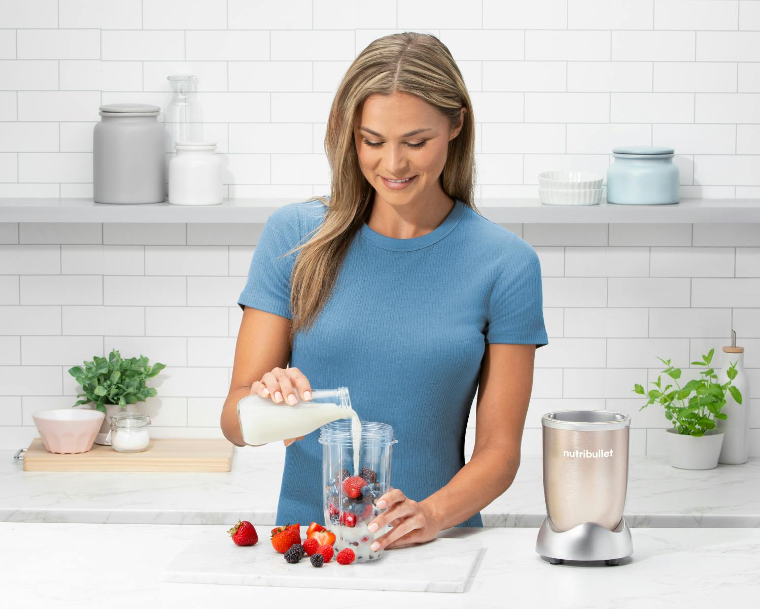 Woman pouring milk in a nutribullet with fruit in the kitchen.